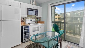 A compact kitchen with white cabinets, a microwave, stove, and a glass-enclosed oven. There's a small dining area with a glass table and chairs, and a balcony with a view of the neighborhood. - 3BR Oceanfront Townhome on North Topsail Beach (North Topsail Beach)