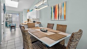 A modern dining area with a white table, woven chairs, and a colorful abstract painting on the wall. - 3BR Oceanfront Townhome on North Topsail Beach (North Topsail Beach)