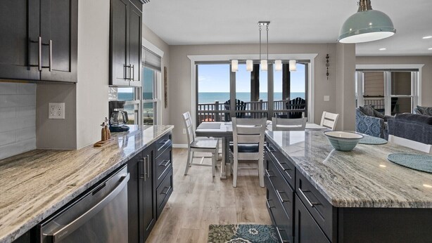 A modern kitchen with a large island, dark cabinetry, and a view to the outside. - 3BR Oceanfront Condo with Community Pool (North Topsail Beach)