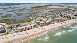 A coastal hotel with multiple buildings, a beach, and a marshy landscape in the background. - 3BR Oceanfront Condo with Community Pool (North Topsail Beach)