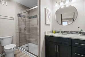 Et moderne badeværelse med en brusekabine i glas, toilet, vaskebord med vask og et spejl.
