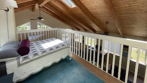 A bedroom with a wooden ceiling, a bed with a floral bedspread, a white railing, and a view of the outdoors. - Bayshore RV Park & Guest Suites (Tokeland)