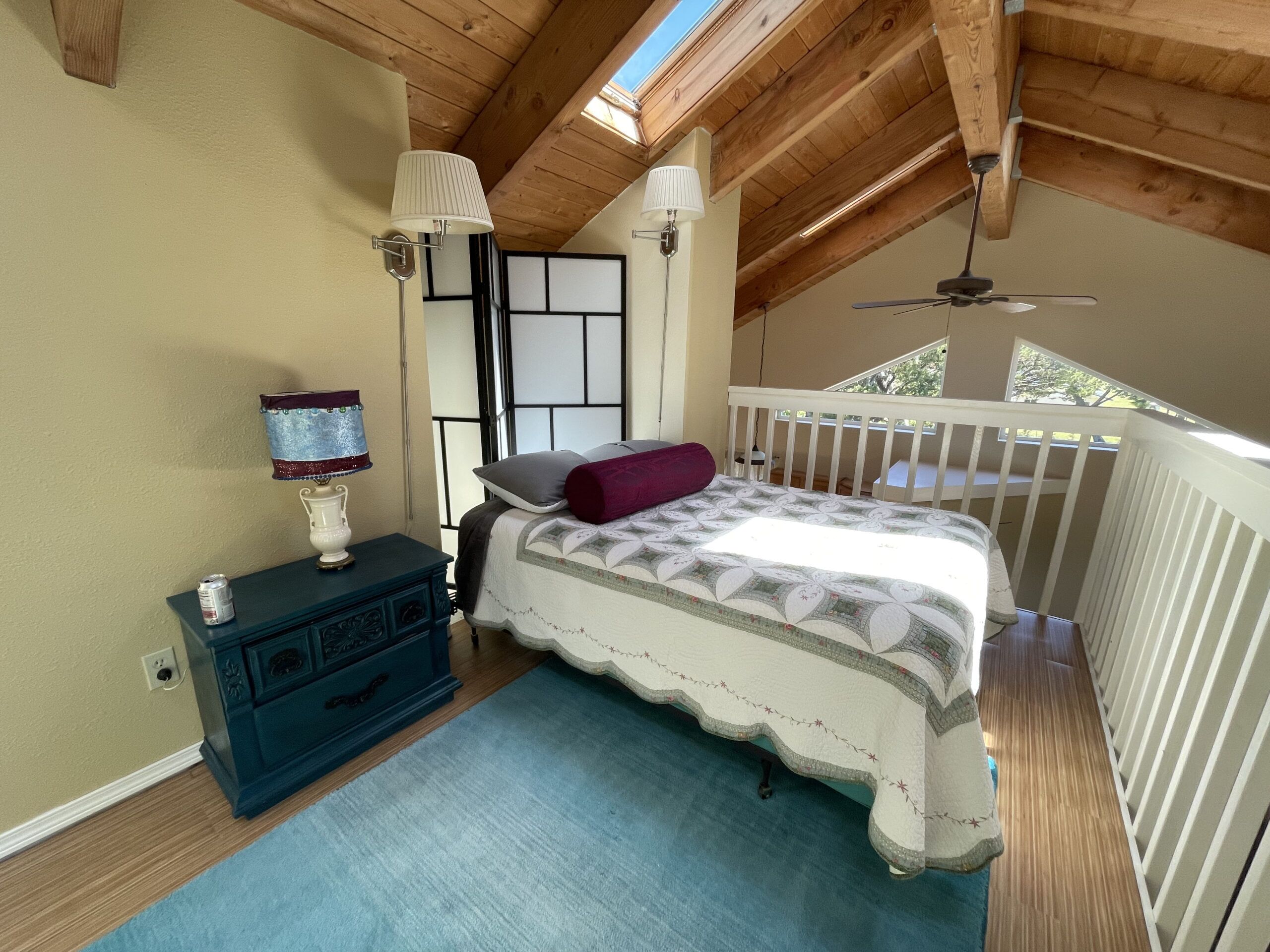 Un dormitorio con cama, cómoda, lámpara y ventilador de techo.