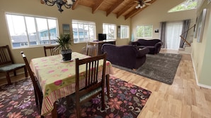 A spacious living area with a high ceiling, wooden beams, a dining table with chairs, a sofa, and a TV. - Bayshore RV Park & Guest Suites (Tokeland)
