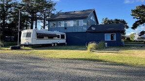 A two-story house with a satellite dish, a white RV parked in front, and a small garden area. - Bayshore RV Park & Guest Suites (Tokeland)