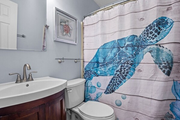A bathroom with a wooden shower curtain featuring a sea turtle design, a white sink, and a toilet.