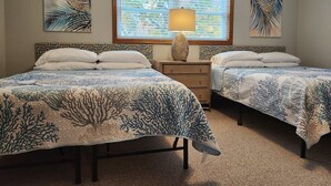 A bedroom with two beds, each with a blue and white coral-patterned bedspread, a window with blinds, and a lamp on a nightstand.