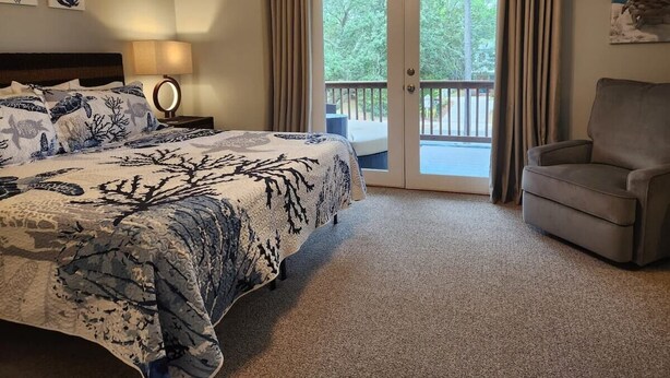 A bedroom with a bed, a chair, a nightstand, and a balcony with curtains.