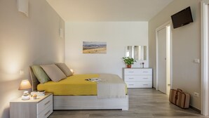 Un dormitorio con cama, mesita de noche, lámpara, cómoda, espejo y maleta.
