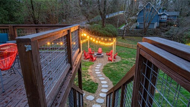 A wooden deck with a stone pathway leading to a seating area with red chairs and a fire pit. - Pet-Friendly, Sauna, Hot Tub, Game Room, Two Firepits, Sleeps 12 (Asheville)