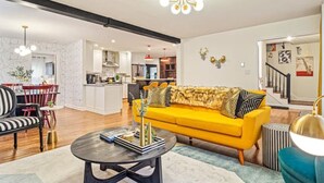 A modern living room with a yellow sofa, a black and white striped sofa, a round coffee table, and a dining area with red chairs. - Pet-Friendly, Sauna, Hot Tub, Game Room, Two Firepits, Sleeps 12 (Asheville)