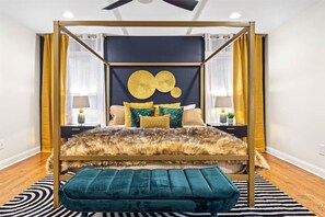 Cama com dossel, manta de pele, banqueta azul-esverdeada e almofadas decorativas.