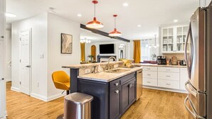 A modern kitchen with a central island, white cabinetry, and a stainless steel refrigerator. - Pet-Friendly, Sauna, Hot Tub, Game Room, Two Firepits, Sleeps 12 (Asheville)