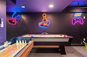 Um quarto com mesa de futebol, mesa de bilhar e luzes de neon em formato de joystick e controle de videogame.