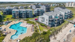 Un quartier résidentiel en bord de mer, avec des immeubles modernes à plusieurs étages, une piscine centrale et une plage.
