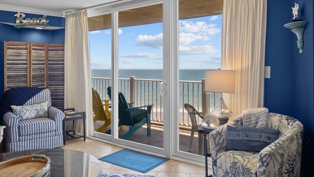 Una habitación con vista al océano, que incluye un sillón a rayas, una silla verde y un sillón estampado.