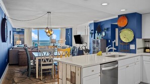 Una cocina moderna con armarios blancos, una isla central y un comedor con vista al océano.