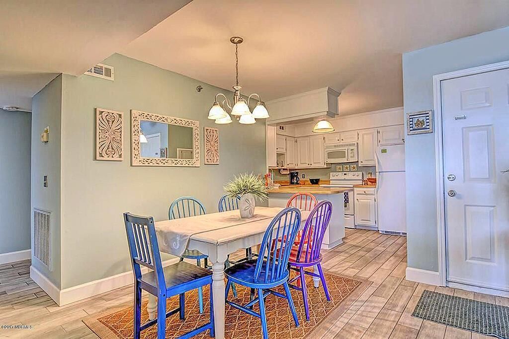A dining area with a table and chairs, a kitchen with white cabinets, and a door.
