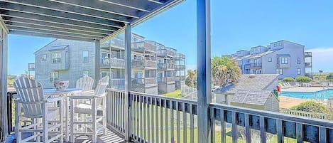 A balcony with a view of a modern building, a pool, and a clear sky.