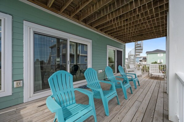 Un porche cubierto con sillas Adirondack turquesa, una terraza de madera y vistas a edificios cercanos.