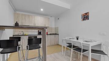 Cocina compacta con comedor, que incluye una mesa y sillas blancas, una cafetera y un mueble pequeño.