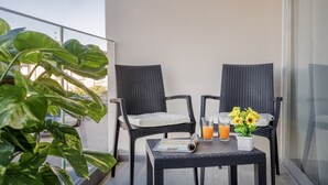 Un balcon avec deux fauteuils en osier, une petite table sur laquelle repose un journal, un verre de jus d’orange et un vase rempli de tournesols.