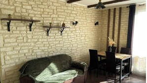 Ein gemütliches Zimmer mit einer Steinwand, einem Holzsofa, einem Esstisch mit Stühlen und einer hängenden Leuchte.