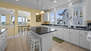 A modern kitchen with a large island, white cabinetry, and a view of the outside. - 5BR Oceanfront Home on North Topsail Sleeps 15 - Pool & Hot Tub (North Topsail Beach)