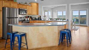 A modern kitchen with wooden cabinets, stainless steel appliances, and a large island with stools. - 5BR Ocean View House on North Topsail Beach - Pool (North Topsail Beach)