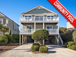 A two-story house with a balcony on the upper floor, a covered front porch, and a small front yard with a tree and shrubs. - 5BR Ocean View House on North Topsail Beach - Pool (North Topsail Beach)