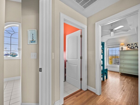 Un couloir avec une porte blanche, un ventilateur de plafond et une vue sur l’extérieur par une fenêtre.