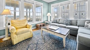 A living room with a yellow armchair, a grey sofa, a coffee table, and a patterned rug. - 4BR Oceanfront House - Sleeps 15 on North Topsail Beach - Pool (North Topsail Beach)