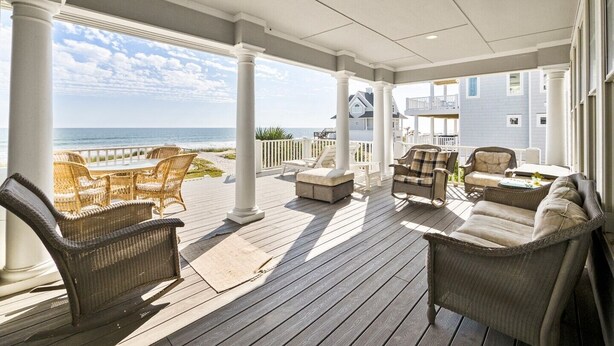 A covered outdoor deck with wicker furniture, a view of the ocean, and a house in the background. - 4BR Oceanfront House - Sleeps 15 on North Topsail Beach - Pool (North Topsail Beach)