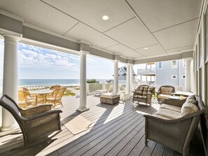A covered outdoor deck with wicker furniture, a view of the ocean, and a house in the background. - 4BR Oceanfront House - Sleeps 15 on North Topsail Beach - Pool (North Topsail Beach)