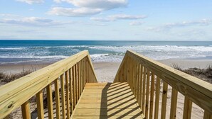 A wooden boardwalk leading to a beach with waves and a clear sky.