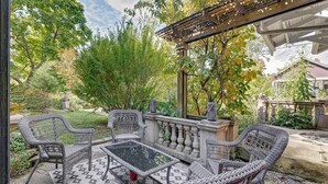 En udendørs terrasse med fletmøbler, et glasbord og et pergola.