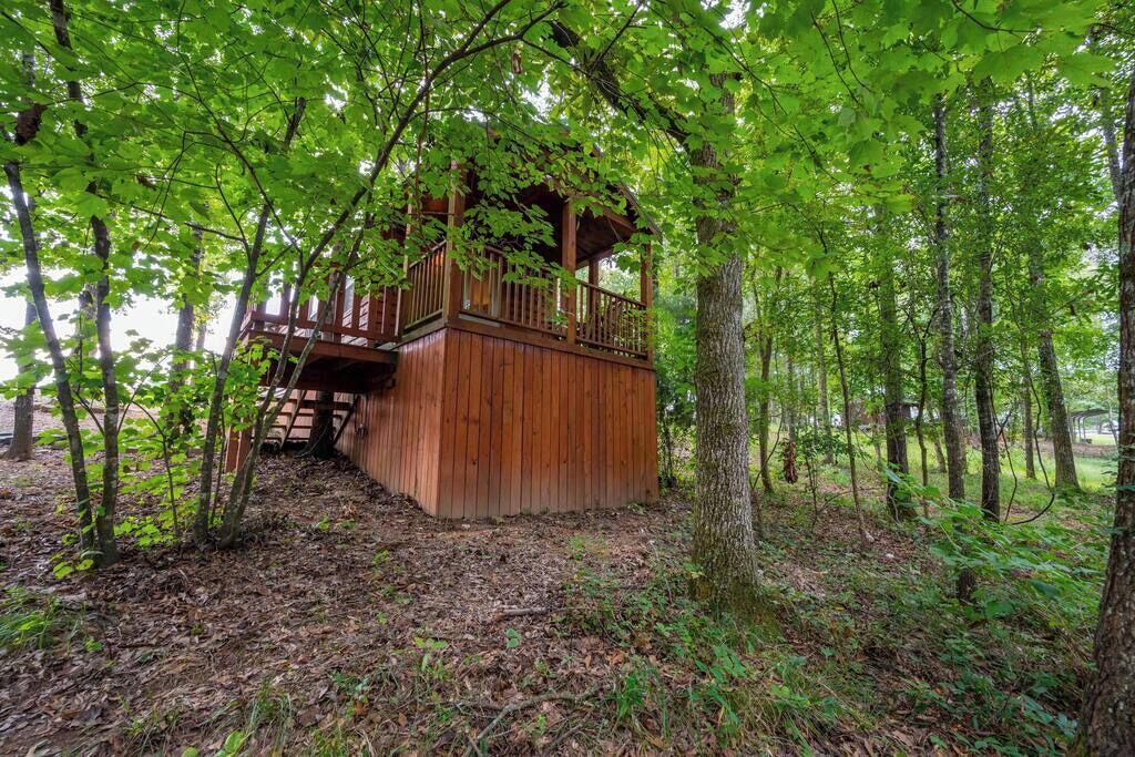 A wooden cabin with a balcony, surrounded by trees and a forest floor.