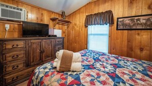 A wooden-paneled room with a bed, dresser, TV, and a window with blinds. - OakLeaf: Sleep 5, Tiny Cabin, Pets, Near Park/Lake (Broken Bow)
