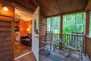 A wooden cabin with a porch, a dining area, and a kitchen visible through an open door.