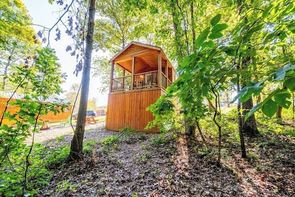 Una cabaña de madera con balcón, rodeada de árboles y un camino de grava.