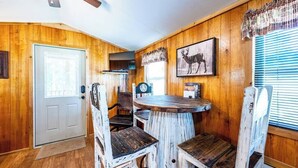 A rustic interior with wooden walls, a round wooden table, and vintage chairs. - PineCone: Sleep 5, Tiny Cabin, Pet, Near Lake/Park (Broken Bow)