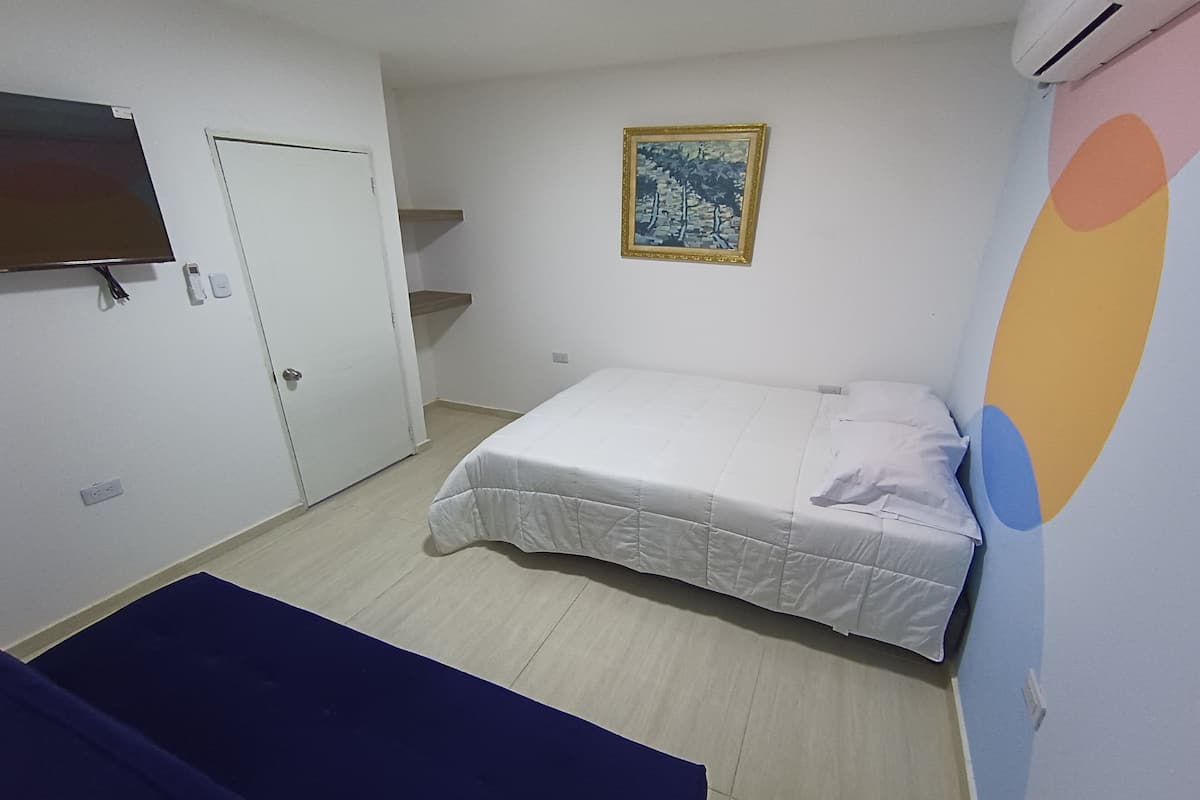 A bedroom with a bed, a TV, a door, and a painting on the wall.