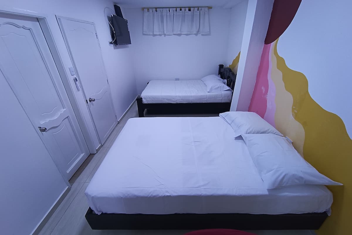 A room with two beds, white bedding, a flat-screen TV mounted on the wall, and a curtain above the beds.