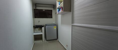 A narrow hallway with a refrigerator, a small sink, and a shelf with bottles.