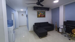 A room with a black sofa, a water dispenser, a ceiling fan, a framed picture, and a desk with a computer. - Ayenda Brisas del Rio (Barranquilla)
