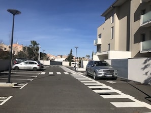 Parkkipaikka täynnä autoja, parvekkeellinen rakennus ja kirkas taivas.