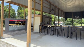 A covered outdoor area with a barbecue grill, seating, and a sign for a pickleball dunk pad. - Gorgeous New 1 bd condo - 5 Min to Branson Landing (Branson)