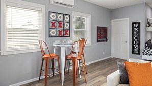 A modern living room with a dining area, featuring a white couch, orange chairs, a round table, and a 'WELCOME' sign. - Gorgeous New 1 bd condo - 5 Min to Branson Landing (Branson)