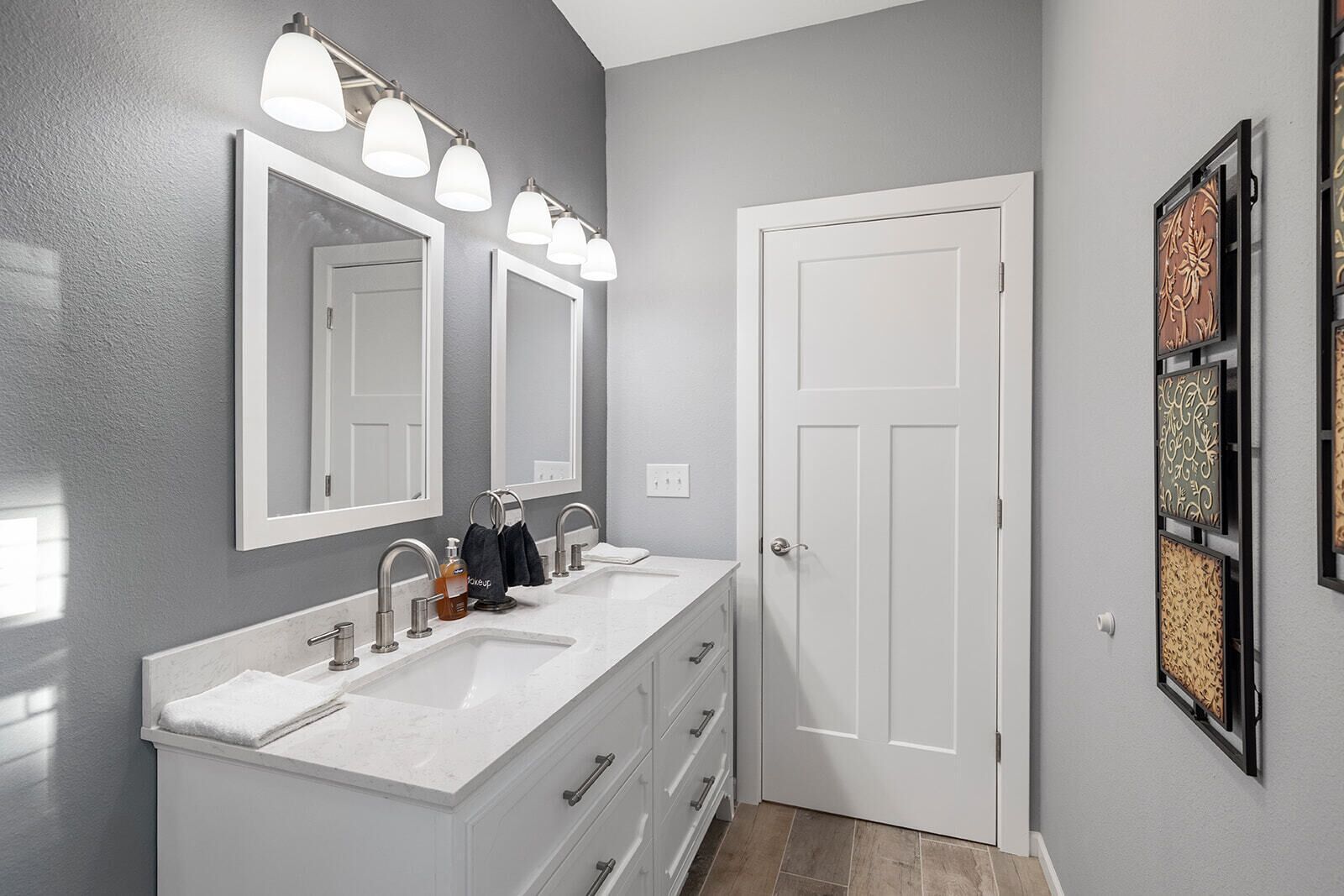 A modern bathroom with a double vanity, a large mirror, and a door with decorative panels.