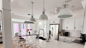 Una cocina amplia con una isla grande, armarios blancos e iluminación colgante.